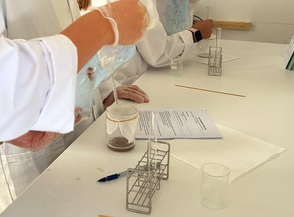 Alumnos de Secundaria con bata y guantes filtran una mezcla de fresa en el laboratorio